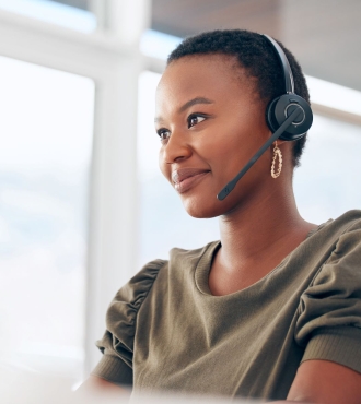 A young, black woman with a small smile is wearing a phone headset, olive-colored blouse and gold earrings.